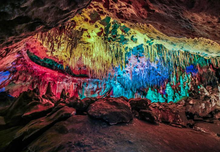 Cave formations on floor and ceiling illuminated by colored lights.